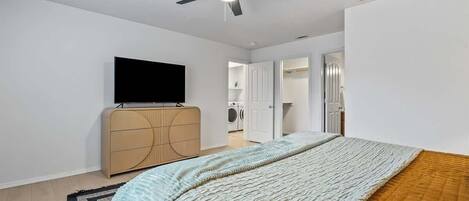 A bedroom with a bed, a ceiling fan, a TV, a wardrobe, and a washing machine in the background.