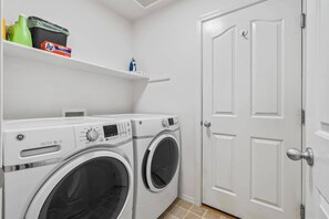 A laundry room with two front-loading washing machines, a shelf with cleaning supplies, and a white door. - Stunning 3BR Home-Backyard HOT TUB Oasis-Home Gym (Boise)