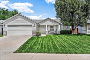 A two-story house with a garage, a well-maintained lawn, and a large tree in front. - Stunning 3BR Home-Backyard HOT TUB Oasis-Home Gym (Boise)