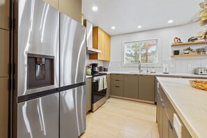 A modern kitchen with stainless steel appliances, wooden cabinets, and a window providing natural light. - Stunning 3BR Home-Backyard HOT TUB Oasis-Home Gym (Boise)