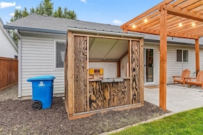 Un espacio al aire libre pequeño y cercado, con una estructura de madera, un basurero y un banco.