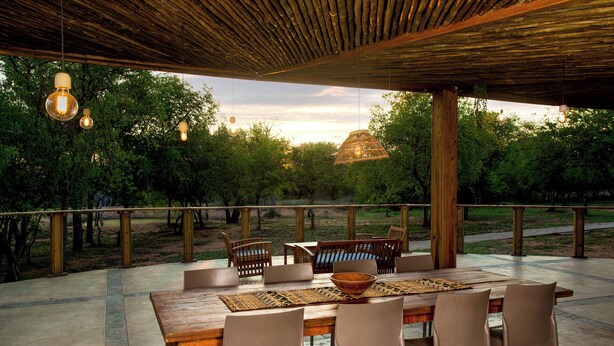 Un área de comedor al aire libre con una mesa y sillas de madera, rodeada por una pérgola de madera con luces colgantes.