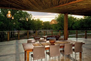 An outdoor dining area with a wooden table and chairs, surrounded by a wooden pergola with hanging lights. - Kubu Bush Lodge (Hoedspruit)