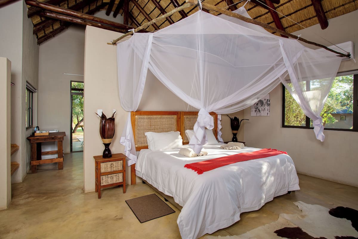 A bedroom with a bed under a mosquito net, a wooden nightstand, a wicker side table, and a cowhide rug.