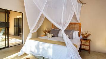 A bedroom with a bed under a white canopy, a wooden nightstand with a woven basket, and a view of a glass door leading outside.