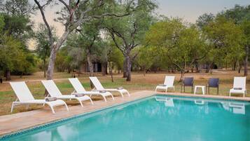 A swimming pool with white lounge chairs and a grassy area with trees.