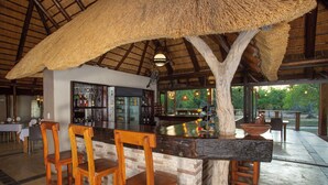 Una zona de bar con sillas de madera, techo de paja y mostrador de ladrillo.