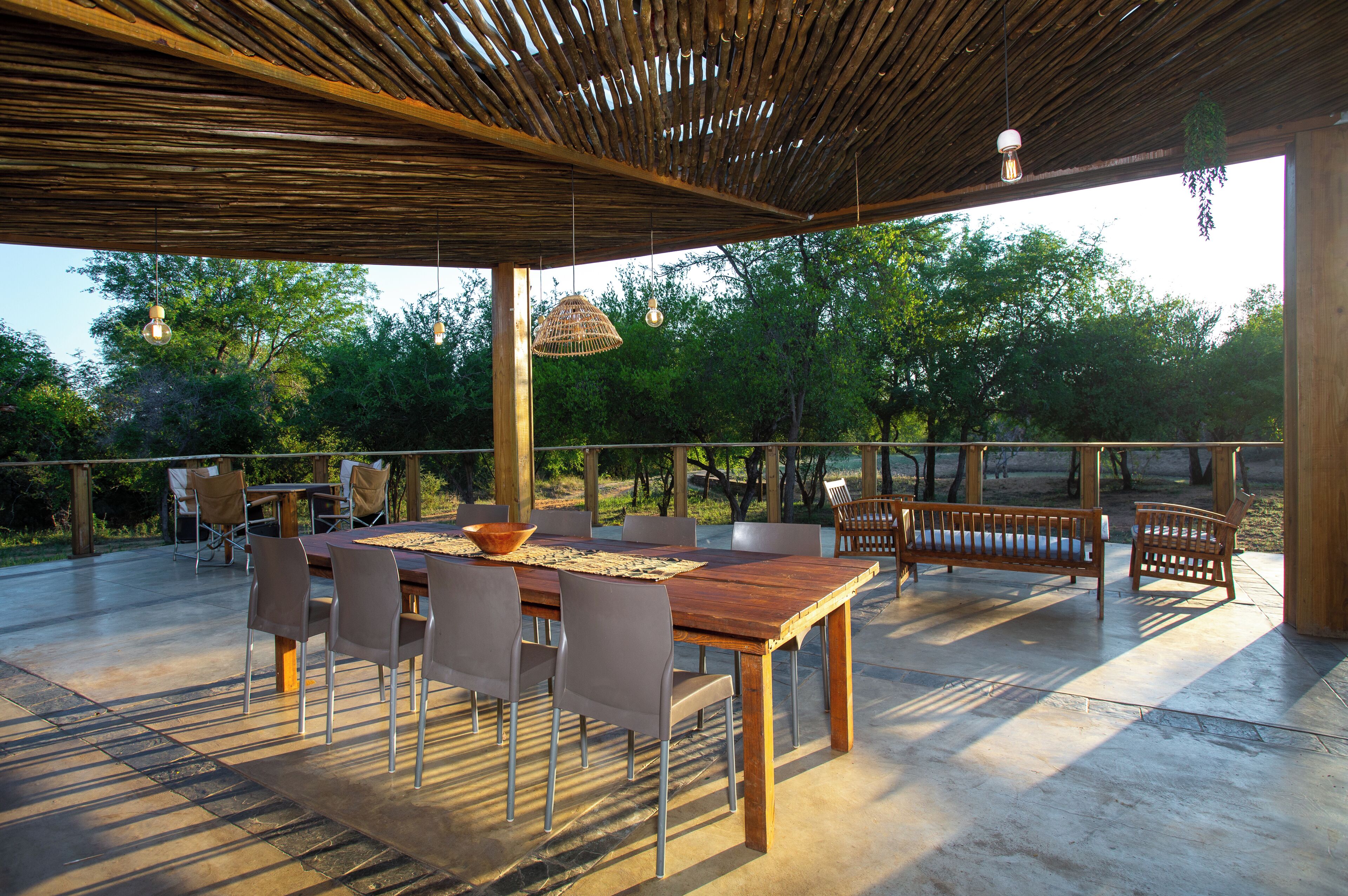 Un patio al aire libre con una mesa y sillas de madera, rodeado por una pérgola con luces colgantes.