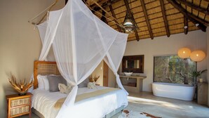 Un dormitorio con cama a dosel, un ventanal grande, una bañera y un tapete de cuero de vaca.