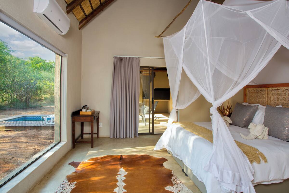 A bedroom with a bed, a window, a desk, and a view of the outdoors.