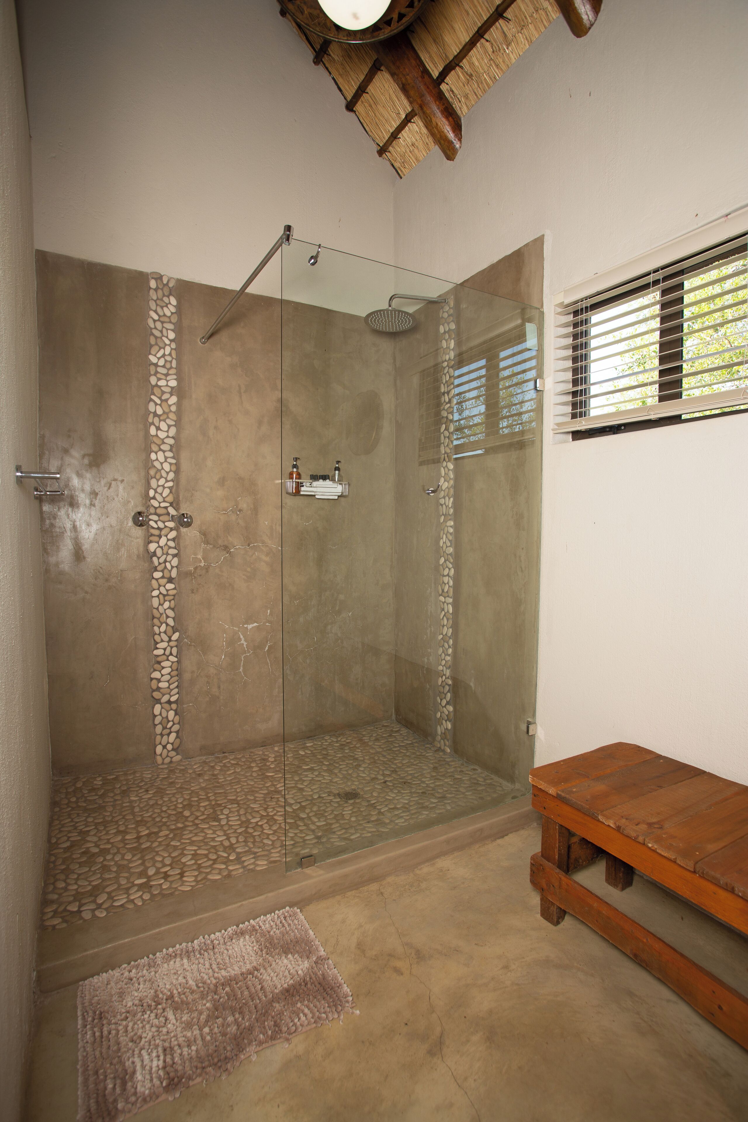 Eine Dusche mit Glastür, eine Holzbank und ein Wandmosaik aus Stein.