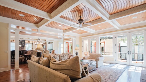 A spacious living area with a high ceiling, wooden beams, and large windows.
