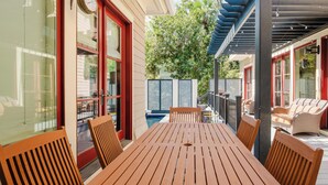 A wooden deck with a table and chairs, a covered area with string lights, and a view of a swimming pool.
