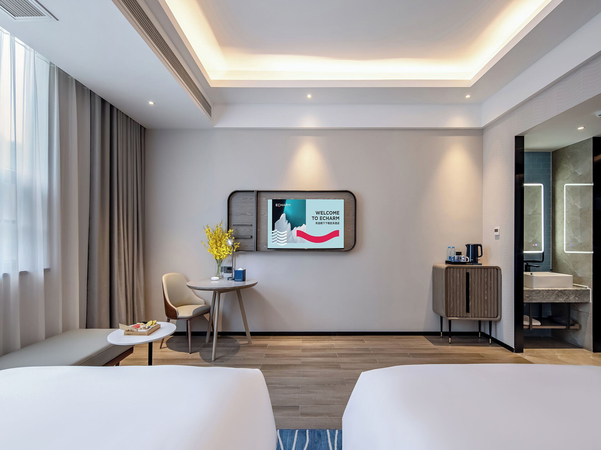Een moderne hotelkamer met een bed, een bureau, een stoel, een kleintje tafeltje met een bloevas, een televisie aan de muur en een badkamer zichtbaar door een geopende deur.