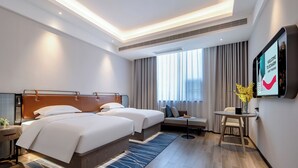 Quarto de hotel com duas camas, uma escrivaninha, uma cadeira, uma televisão e uma janela grande com cortinas.