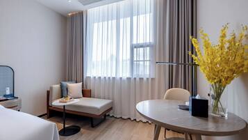 Una habitación de hotel moderna con una cama, un sofá, una mesa redonda y una ventana con cortinas.