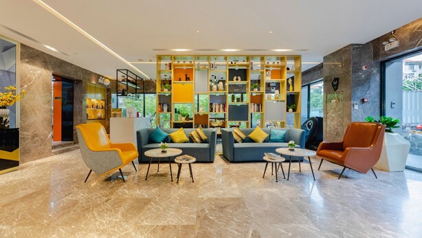 Un hall d’entrée moderne avec deux canapés, un fauteuil jaune et un fauteuil marron. On y trouve des étagères remplies de livres et d’objets décoratifs.