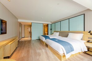 A hotel room with a wooden floor, two beds with blue and white bedding, a wooden desk with a lamp, and a TV on the wall. - yishangjiudiannanningqingxiushandian (Nanning)