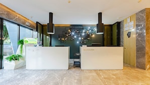 Un espace d’accueil avec deux comptoirs de réception blancs portant l’inscription « ECHARM », un luminaire fixé au mur et une plante en pot.