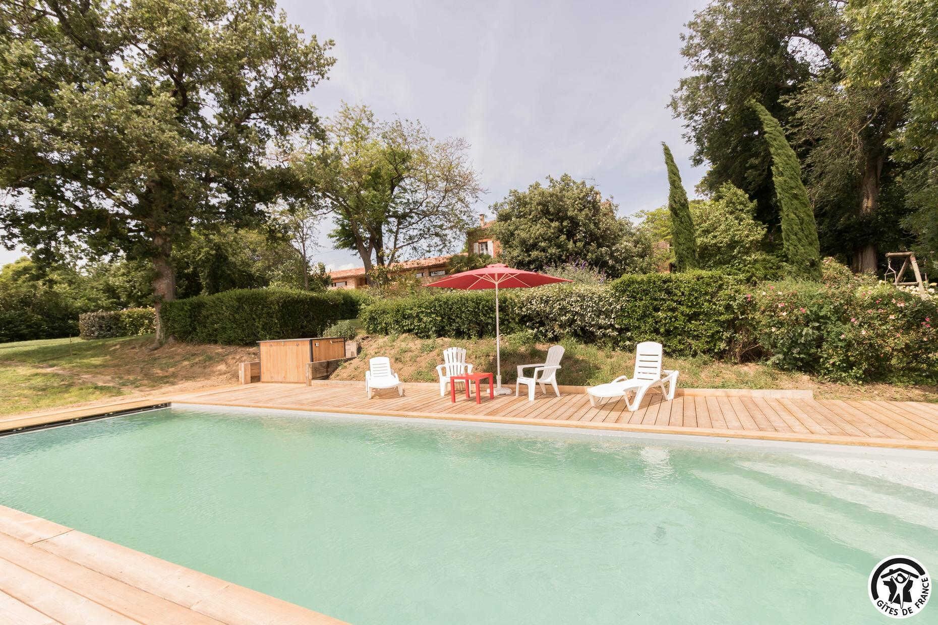 Una piscina con cubierta de madera, rodeada de follaje y árboles.