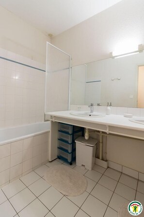 Een badkamer met twee wastafels, een spiegel, een badkuip en opbergladen.