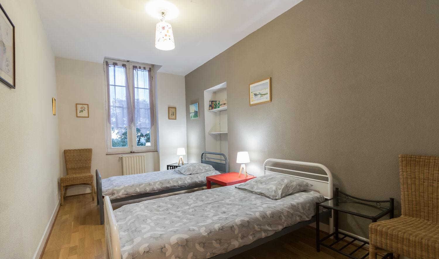 A room with two beds, a window, a chair, and a table.