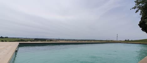 Una piscina rectangular con borde de hormigón, rodeada de césped y una vista distante de una torre de líneas eléctricas.