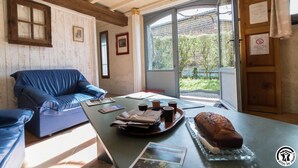 Quarto aconchegante com teto de madeira, sofá azul, mesa com um croissant e vista para o verde lá fora.