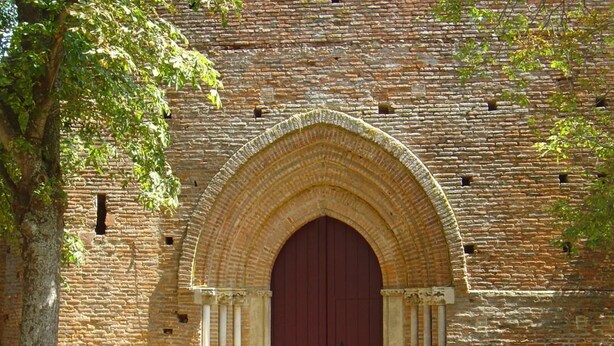 Um edifício de tijolos com uma grande entrada em arco e uma porta vermelha.