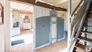 Interior rústico com escada de madeira, porta azul e chão de azulejos.