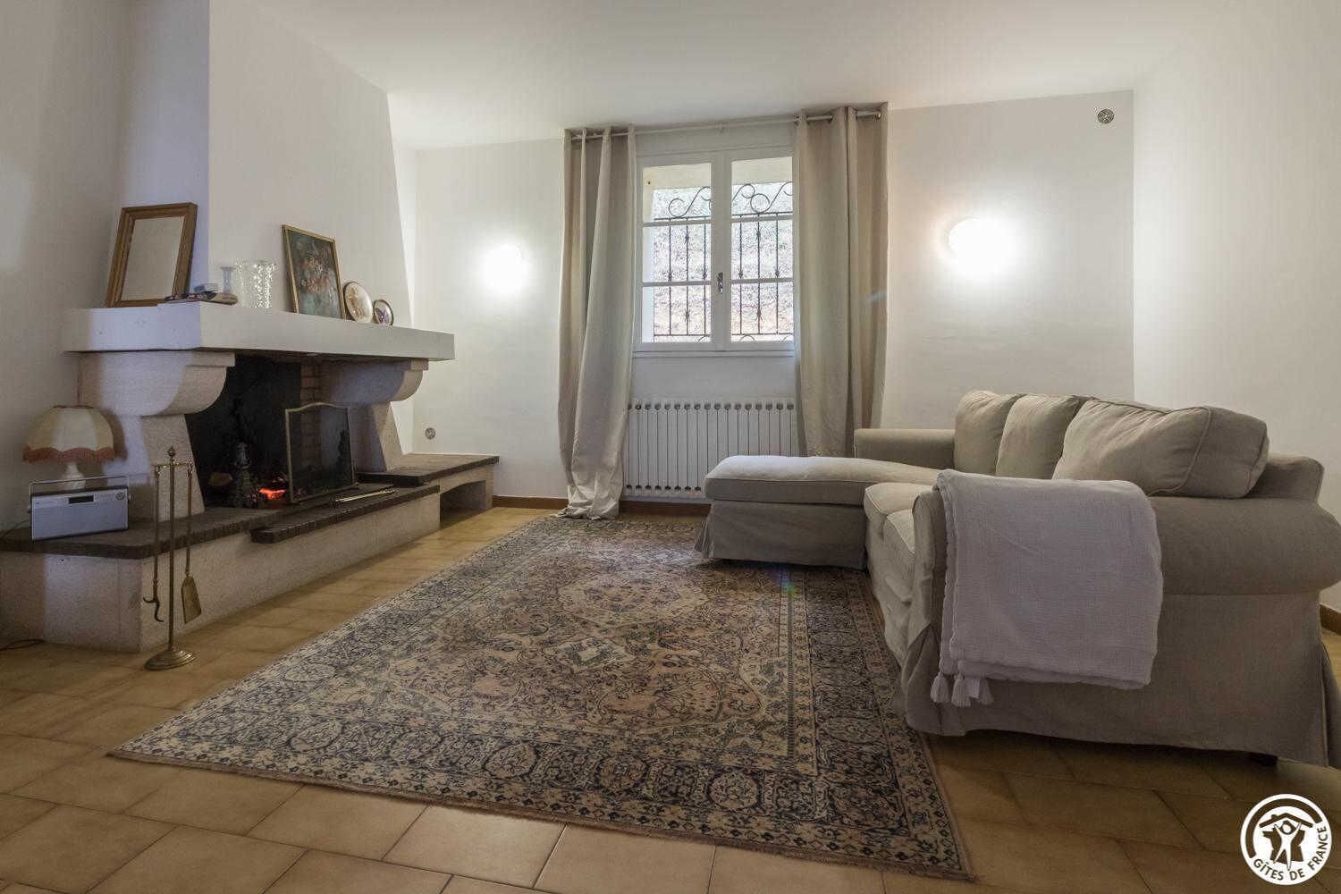 A living room with a fireplace, a sofa, a patterned rug, and a window with curtains.