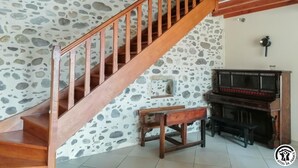A staircase with wooden railings leading to a room with a stone wall, a piano, and a bench.