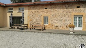 A stone building with a tiled roof, a gravel driveway, and outdoor seating.