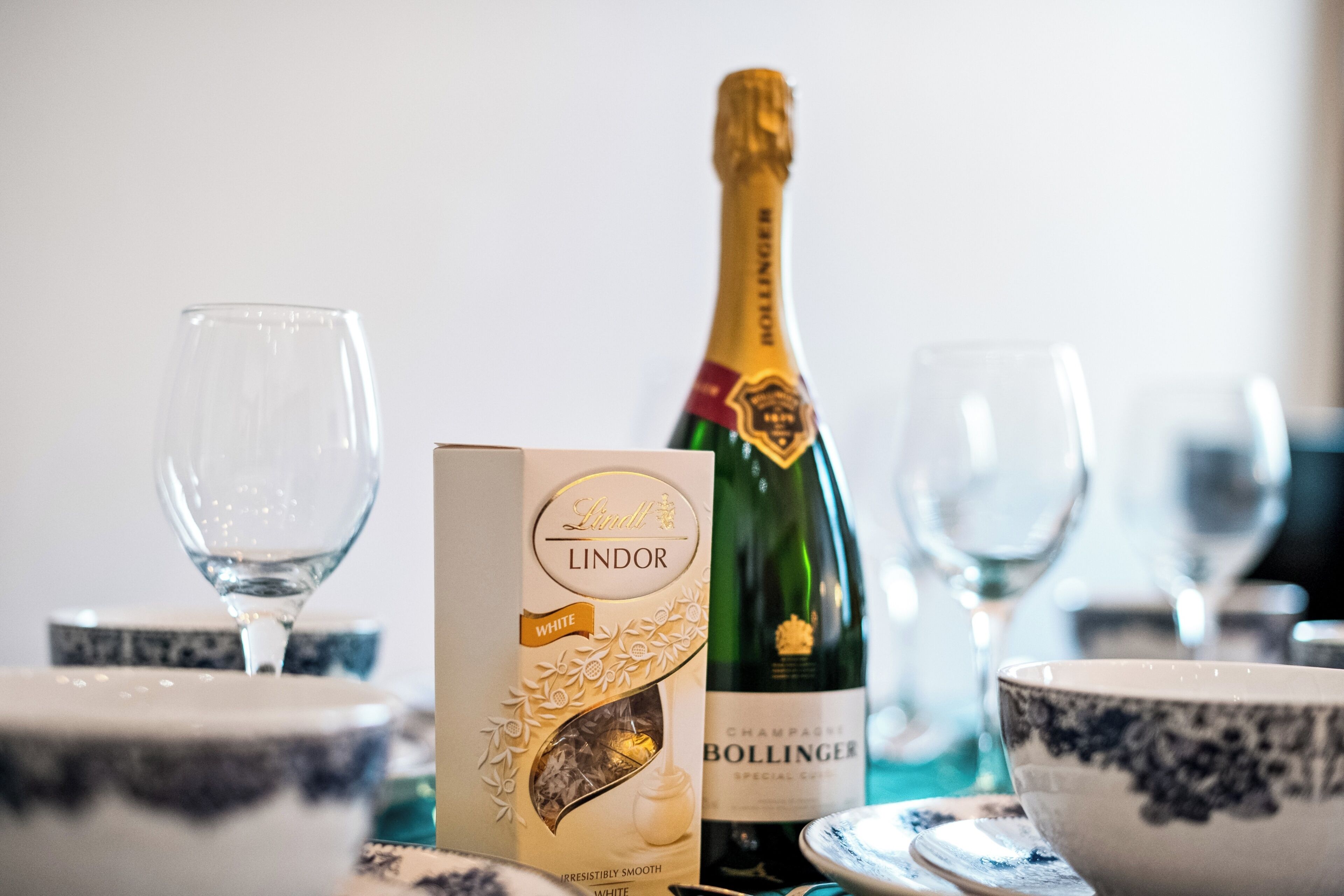 Una mesa dispuesta con una botella de champán Bollinger, una caja de bombones Lindor y varias copas de vino vacías.