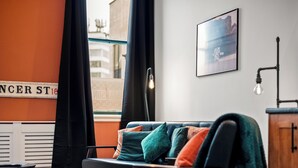 A modern living room with a sofa, a view of the street, and a framed picture on the wall. - 3 Bed Flat - Sleeps 7 - Parking - Wifi (Birmingham)