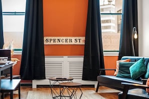 A room with a black sofa, a small round table, and a window with black curtains. - 3 Bed Flat - Sleeps 7 - Parking - Wifi (Birmingham)