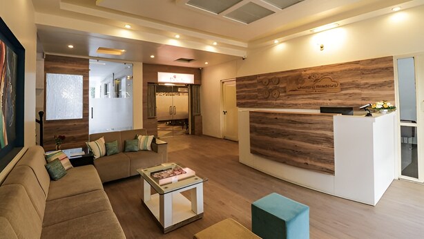 A modern living room with a sofa, coffee table, and a reception desk with a wooden accent wall. - Arristo Resorts & Club (Ahmedabad)