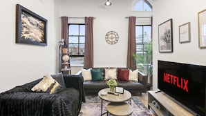 A modern living room with a sofa, coffee table, and a flat-screen TV displaying "NETFLIX".