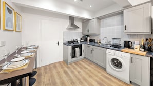 A modern kitchen with grey cabinets, a built-in oven, a washing machine, and a dining area with a table set for four.