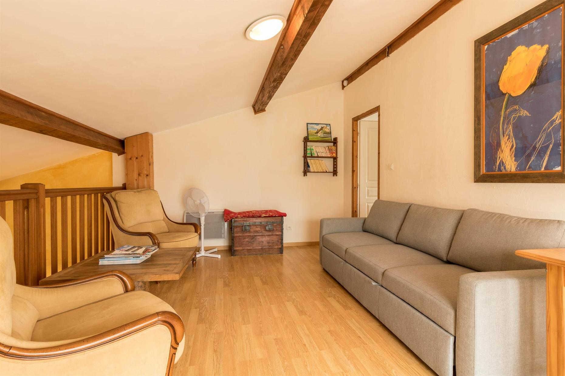 Un soggiorno accogliente con soffitto in legno, un divano grigio, un tavolino da caffè in legno e una poltrona beige.