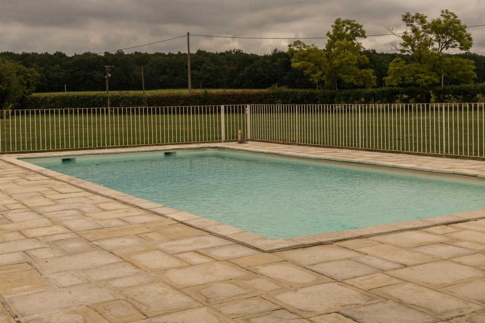 A rectangular swimming pool with a tiled deck, surrounded by a white fence.