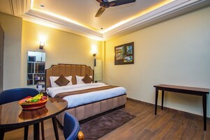 Una habitación de hotel con cama, escritorio, silla, una mesa con fruta y un ventilador de techo.