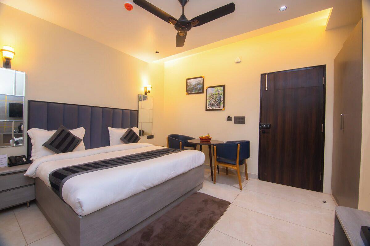 A modern hotel room with a large bed, a desk, a chair, a ceiling fan, and a door.