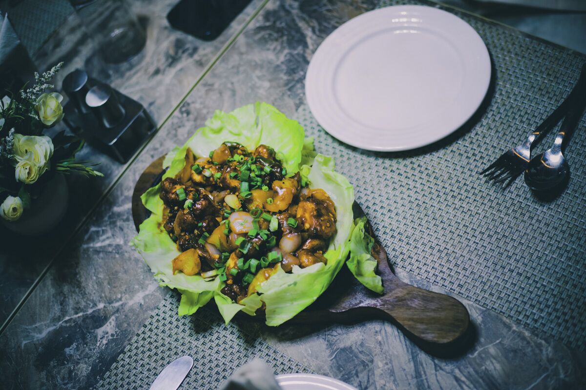 A table with a dish on lettuce, a white plate, and cutlery.