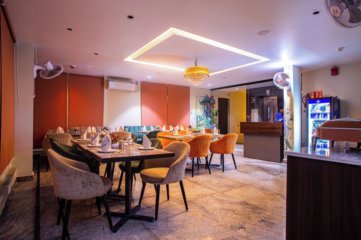 Un restaurante con una decoración moderna, que incluye un comedor con una mesa larga y múltiples sillas, una zona de bar y un mural colorido en la pared.