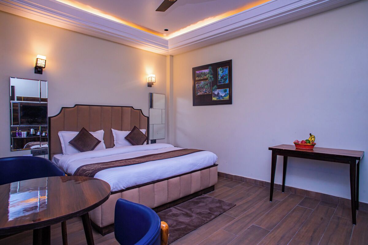 Habitación de hotel con cama, mesita de noche, silla y una pequeña mesa con fruteros.