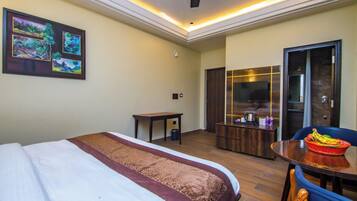 A hotel room with a bed, a desk, a dining table with fruit, a TV, and a sliding door.