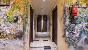 A hallway with a waterfall mural on the walls, a fire extinguisher mounted on the wall, and a potted plant at the end. - Hotel Lords Valley Rishikesh (Rishikesh)