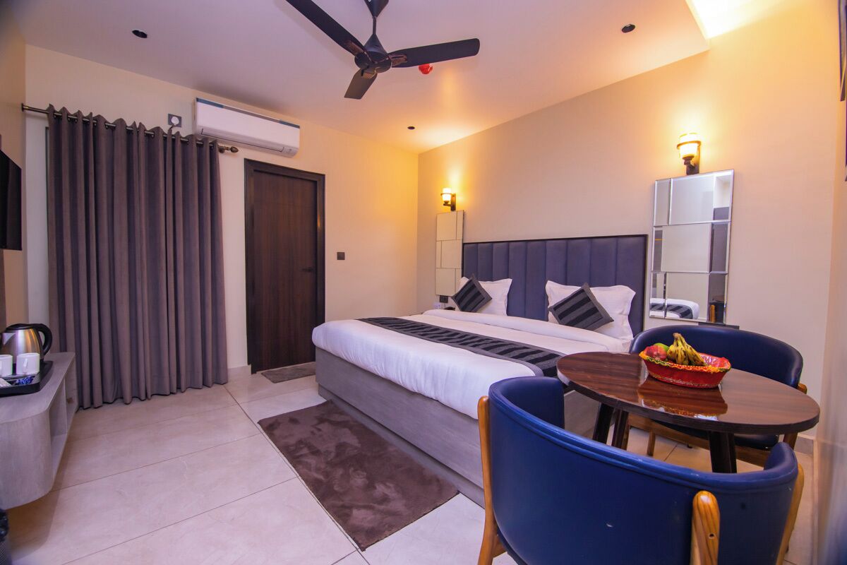 Quarto de hotel com cama, mesa de cabeceira, cadeira e pequena mesa de jantar com uma tigela de fruta.