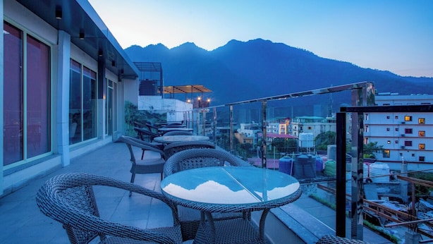 A terrace with wicker furniture and a glass table, overlooking a mountainous landscape. - Hotel Lords Valley Rishikesh (Rishikesh)